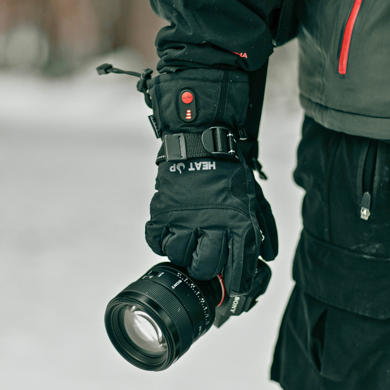 Person wearing heated gloves holding a camera lens in a snowy environment