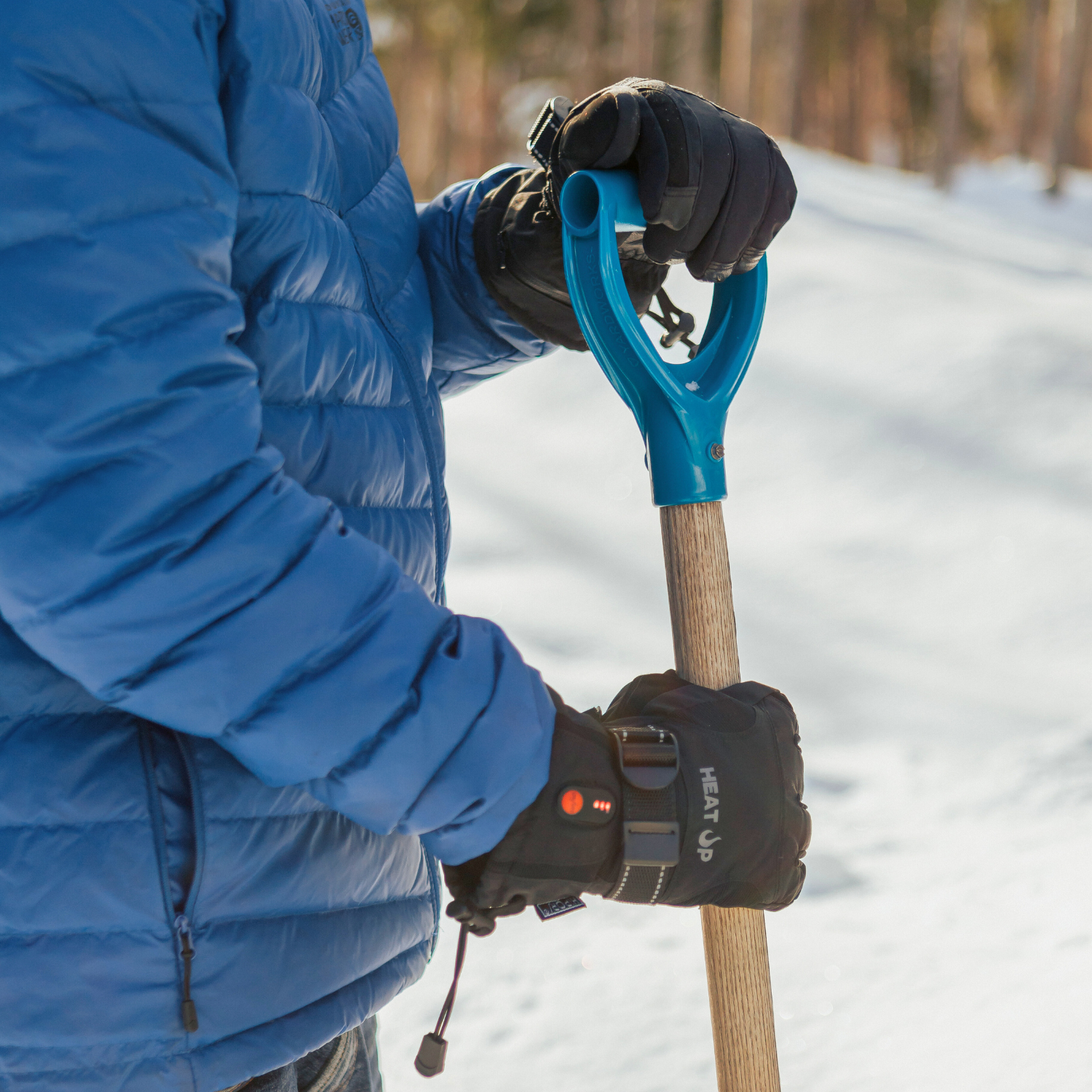 Person holding a snow shovel with a blue handle in a snowy landscape