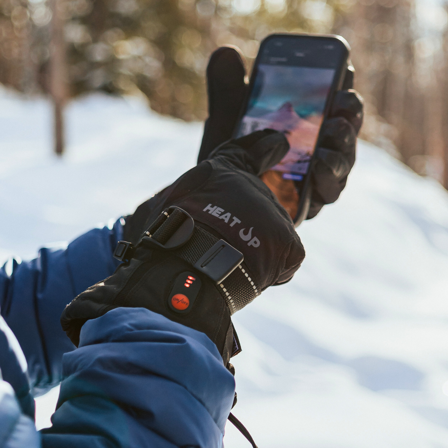 Person wearing heated gloves using a smartphone in a snowy landscape