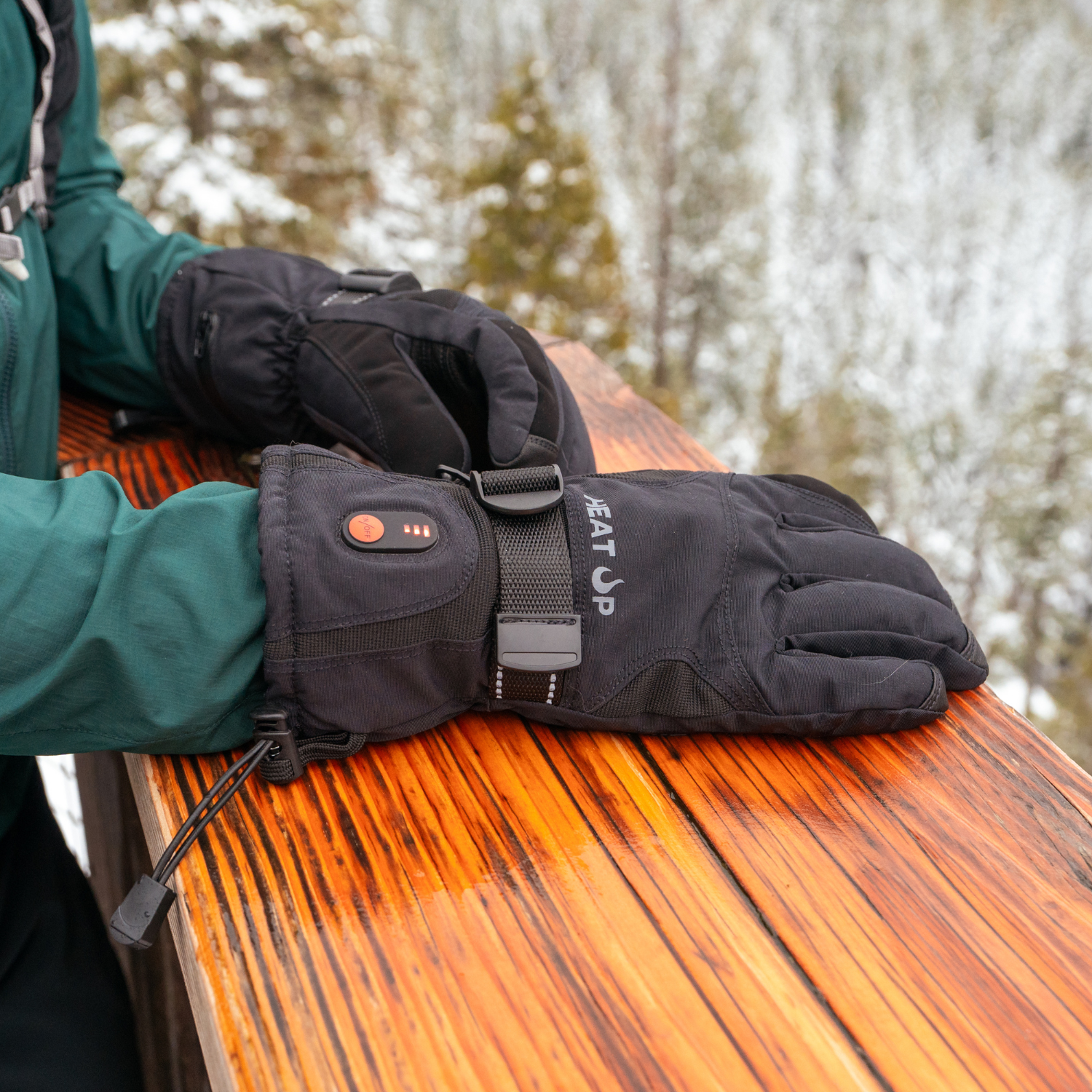Black heated gloves on a wooden surface with a blurred natural background