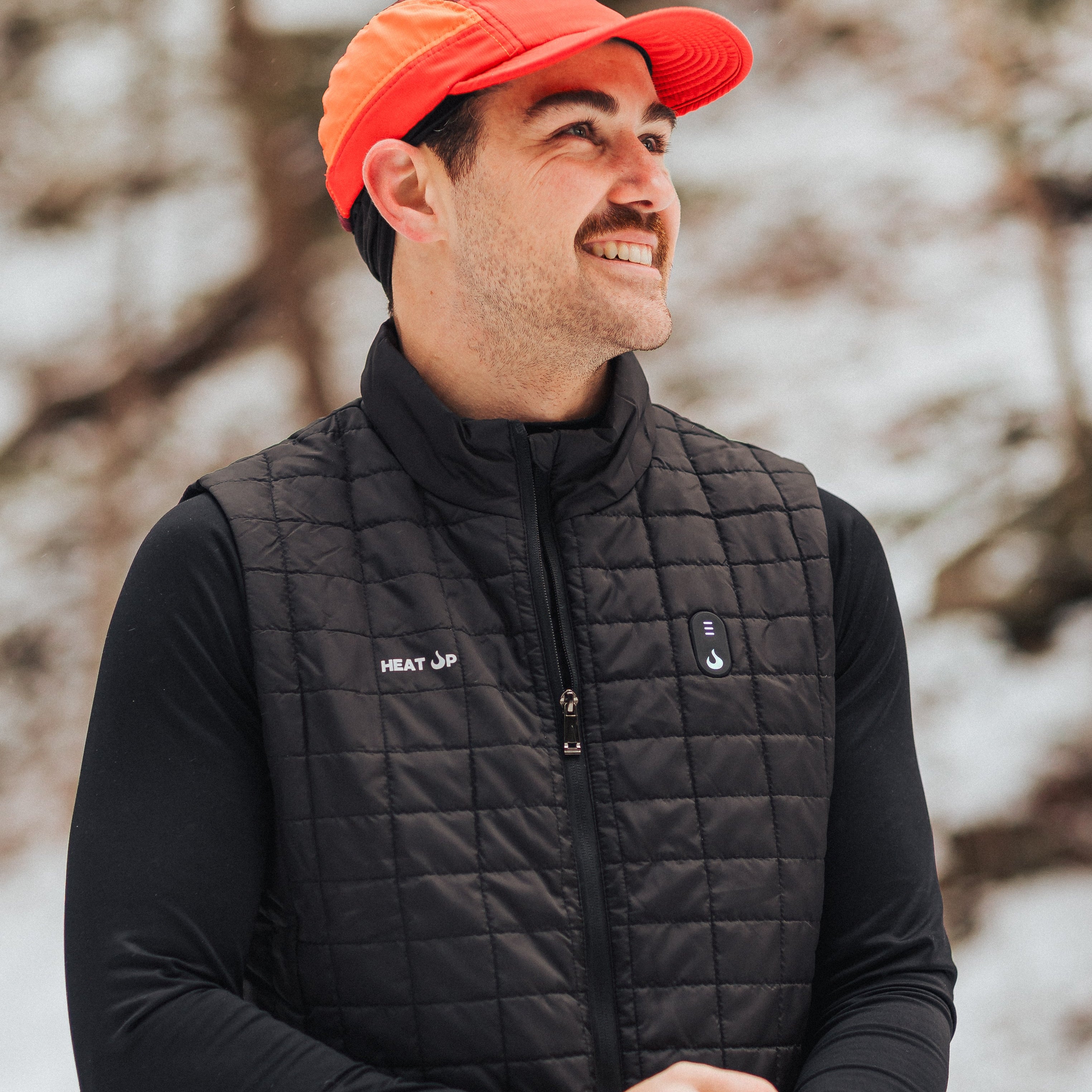 Man wearing a black quilted jacket and orange cap in a snowy outdoor setting