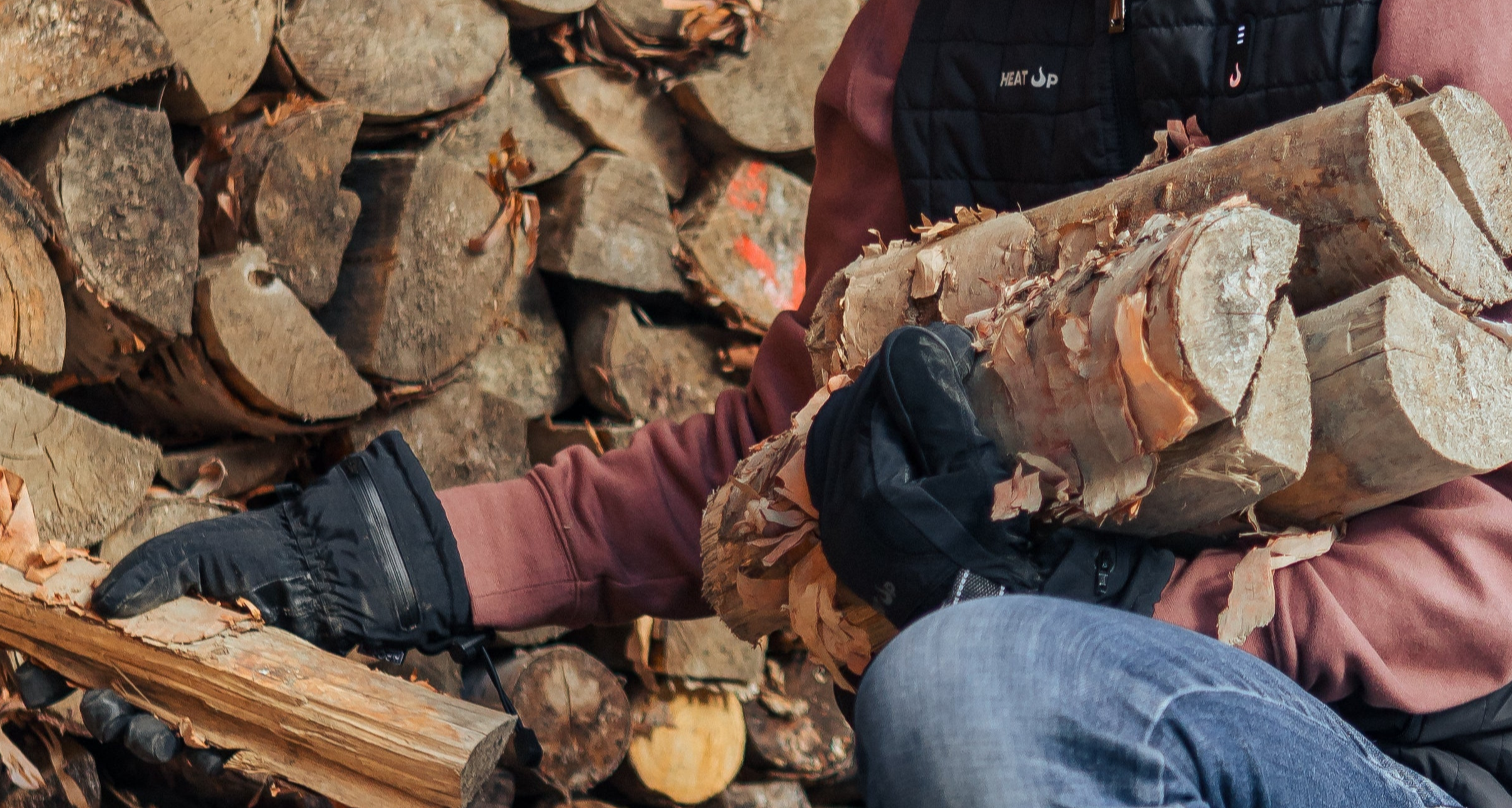 Person splitting wood with a axe against a background of stacked logs