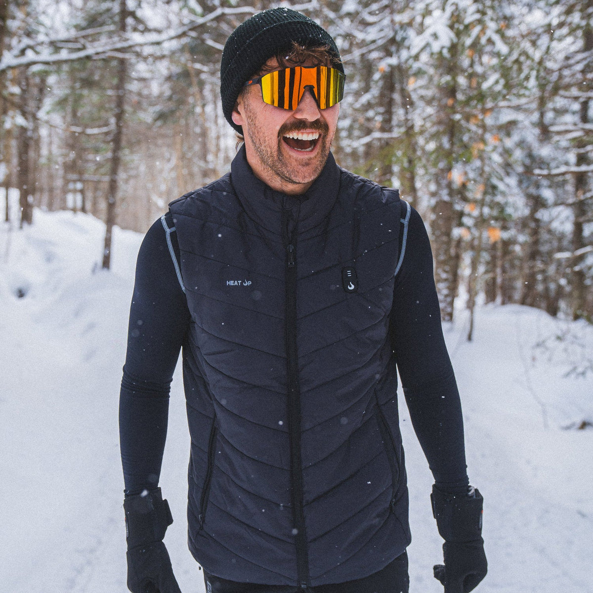 Smiling man in sport sunglasses wearing the Heat Up men's heated vest on a snowy forest trail