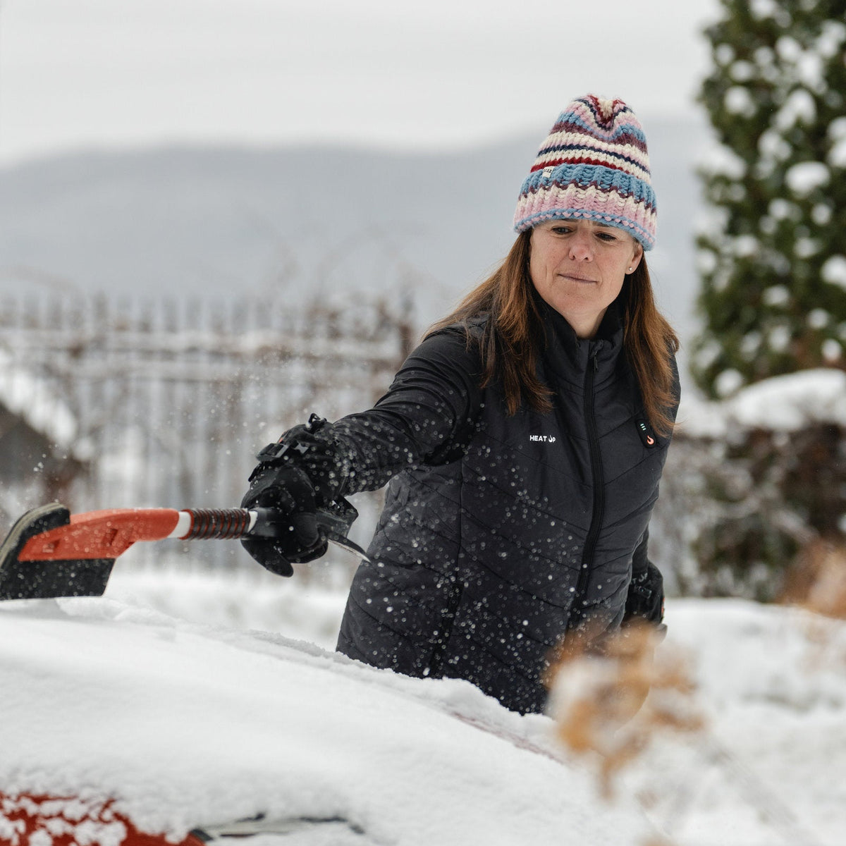 Woman wearing the Heat Up women's heated vest while brushing snow off a car