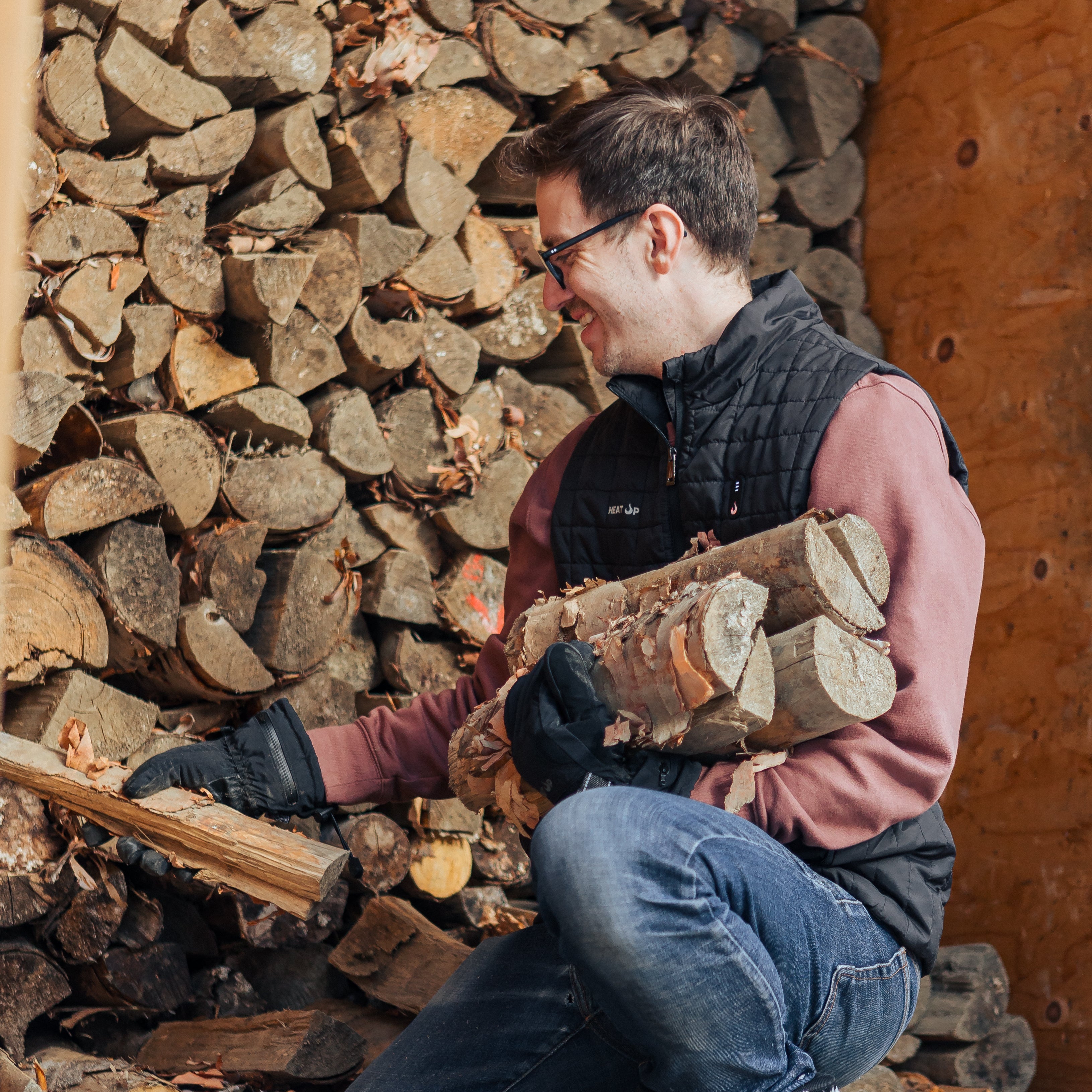 Man carrying a bundle of firewood in front of stacked logs