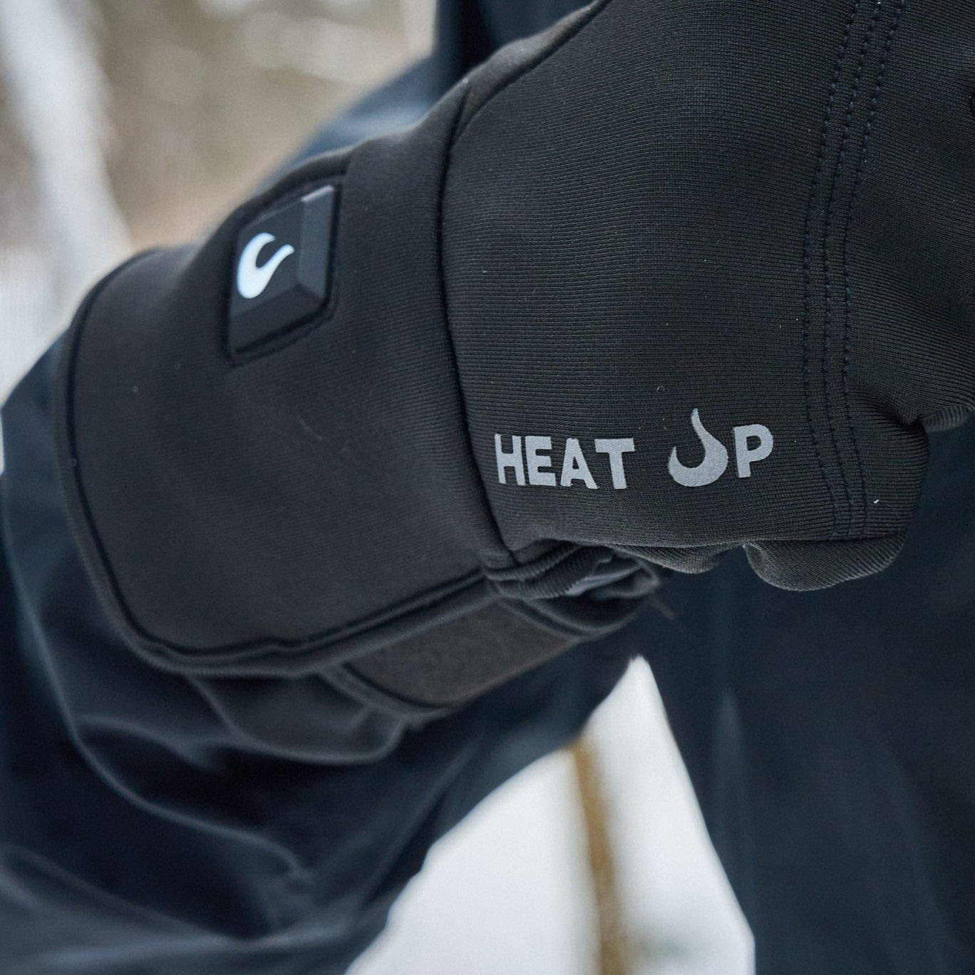 Black heated glove with 'HEAT SP' branding on a blurred outdoor background
