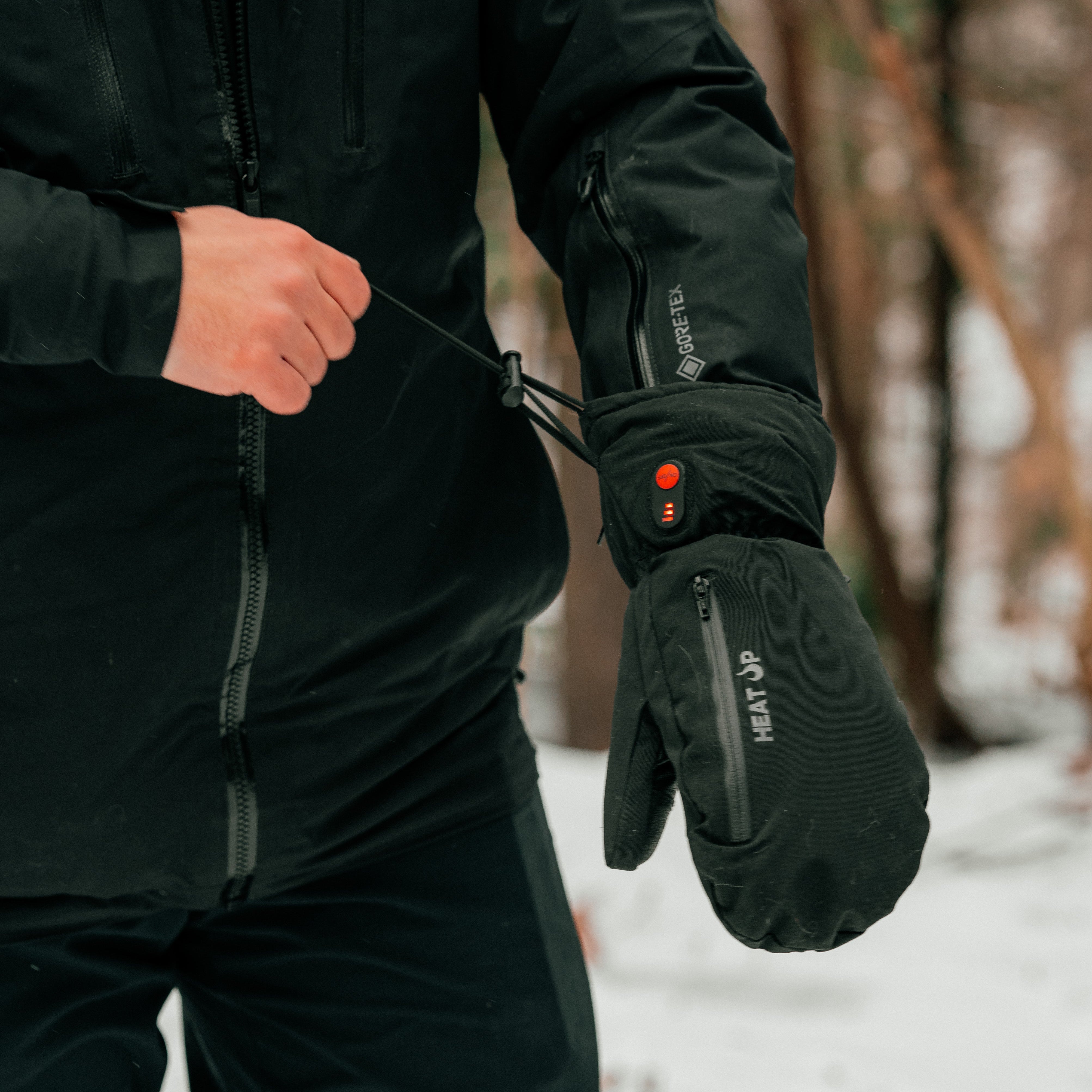Person wearing black heated gloves and jacket in a snowy outdoor setting