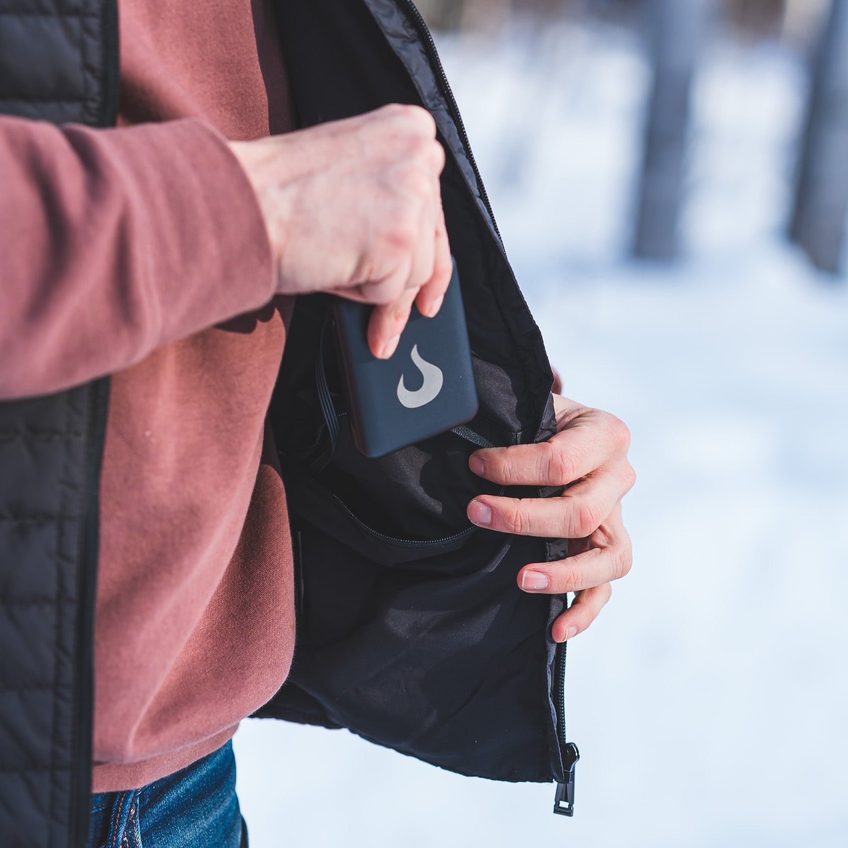 Person holding a black bag with a logo in a snowy outdoor setting