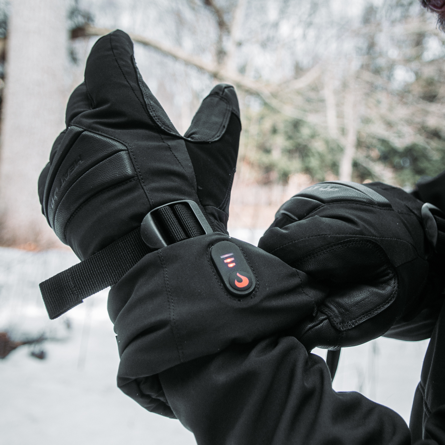 Black insulated gloves with a brand logo held together in a snowy outdoor setting