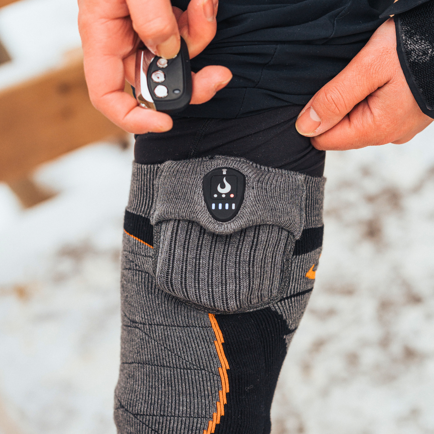 Person wearing heated socks with a control device in a snowy outdoor setting