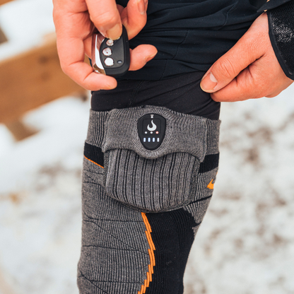 Person wearing heated socks with a control device in a snowy outdoor setting