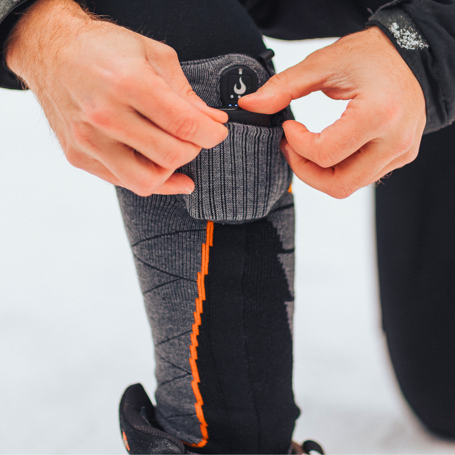 Person adjusting a gray heated sock with orange accents on a white background