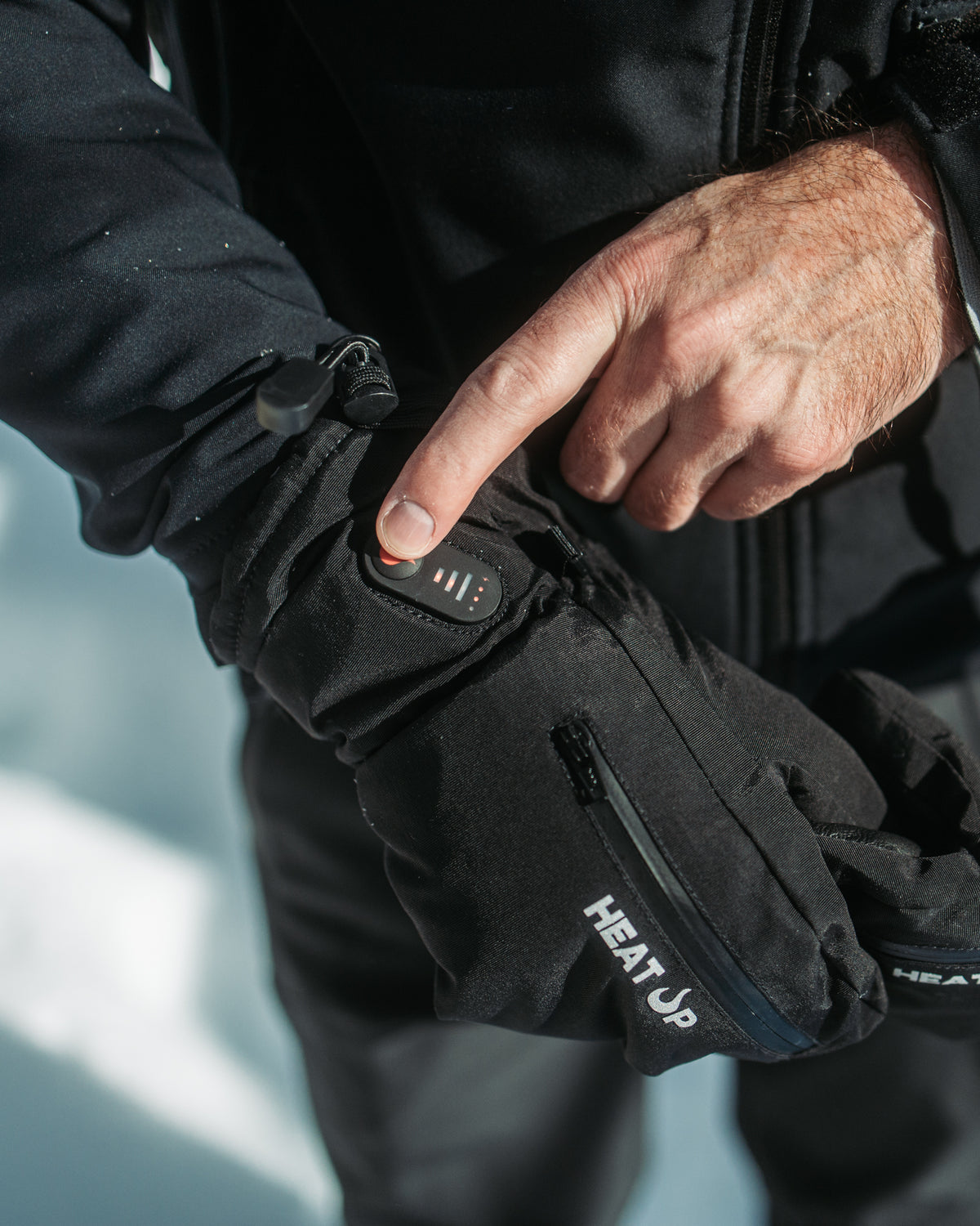 Person pointing at the heat level button on the cuff of a Heat Up heated glove