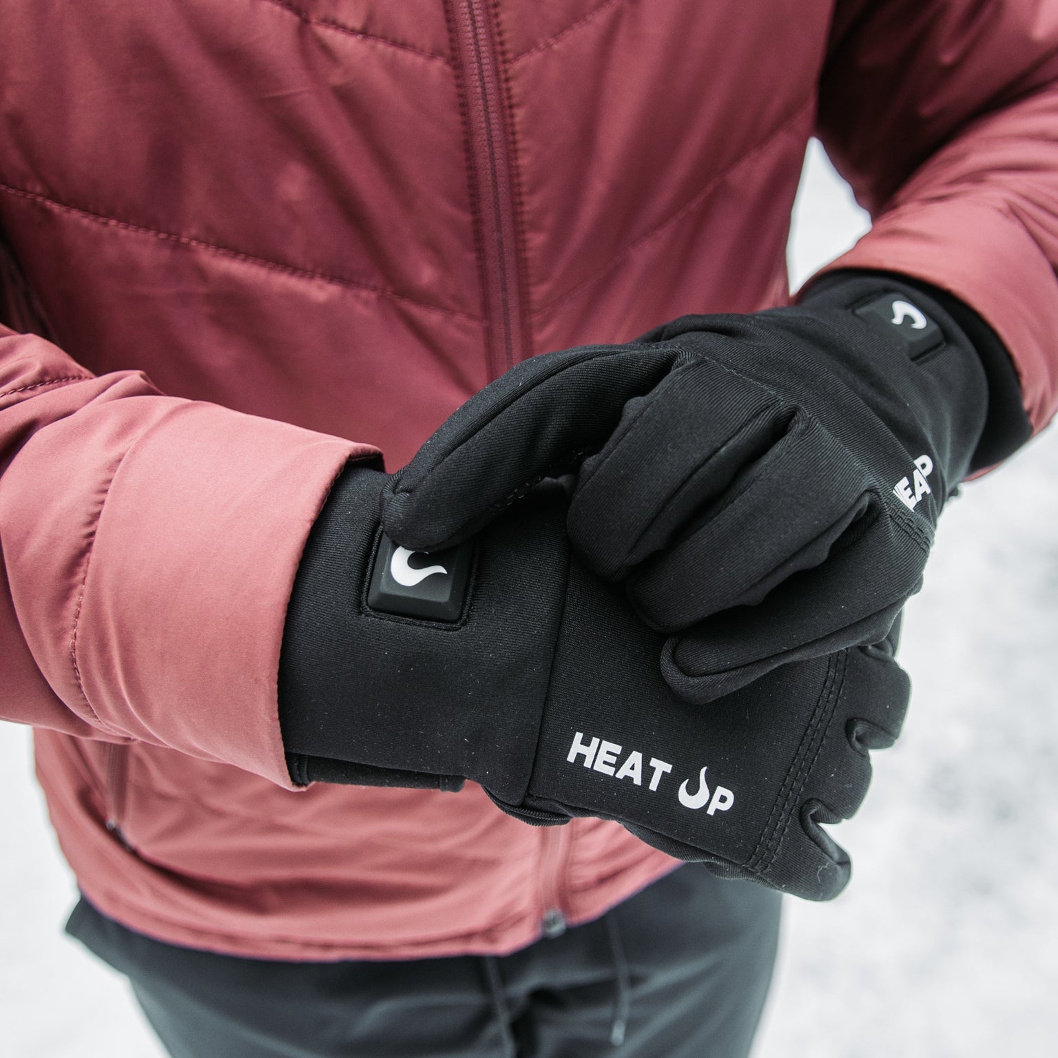 Person wearing black gloves with 'HEAT UP' branding in a snowy setting