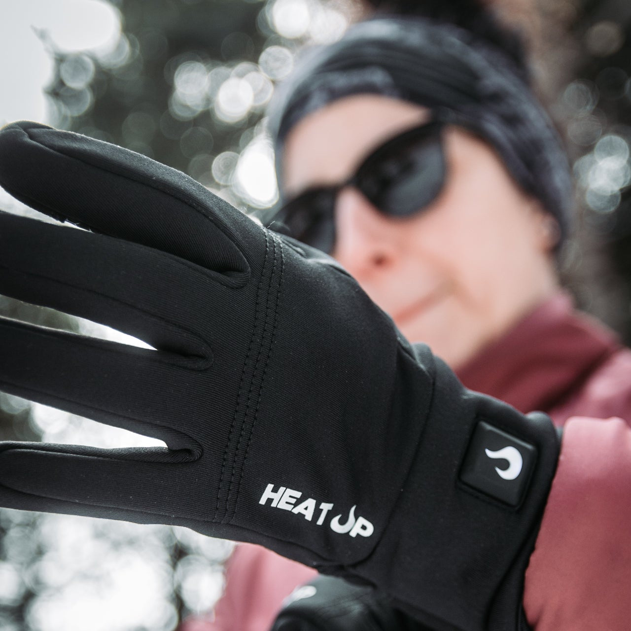 Person wearing black gloves with 'HEAT UP' branding in a snowy outdoor setting