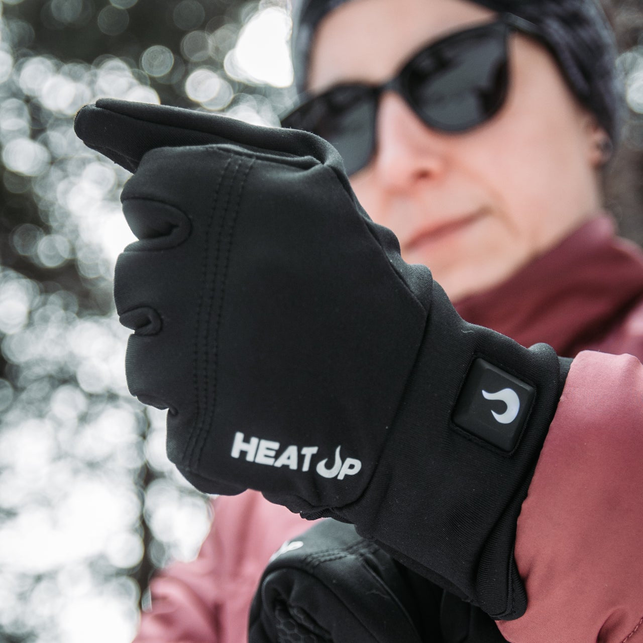 Person wearing black 'HEAT UP' gloves with a blurred outdoor background