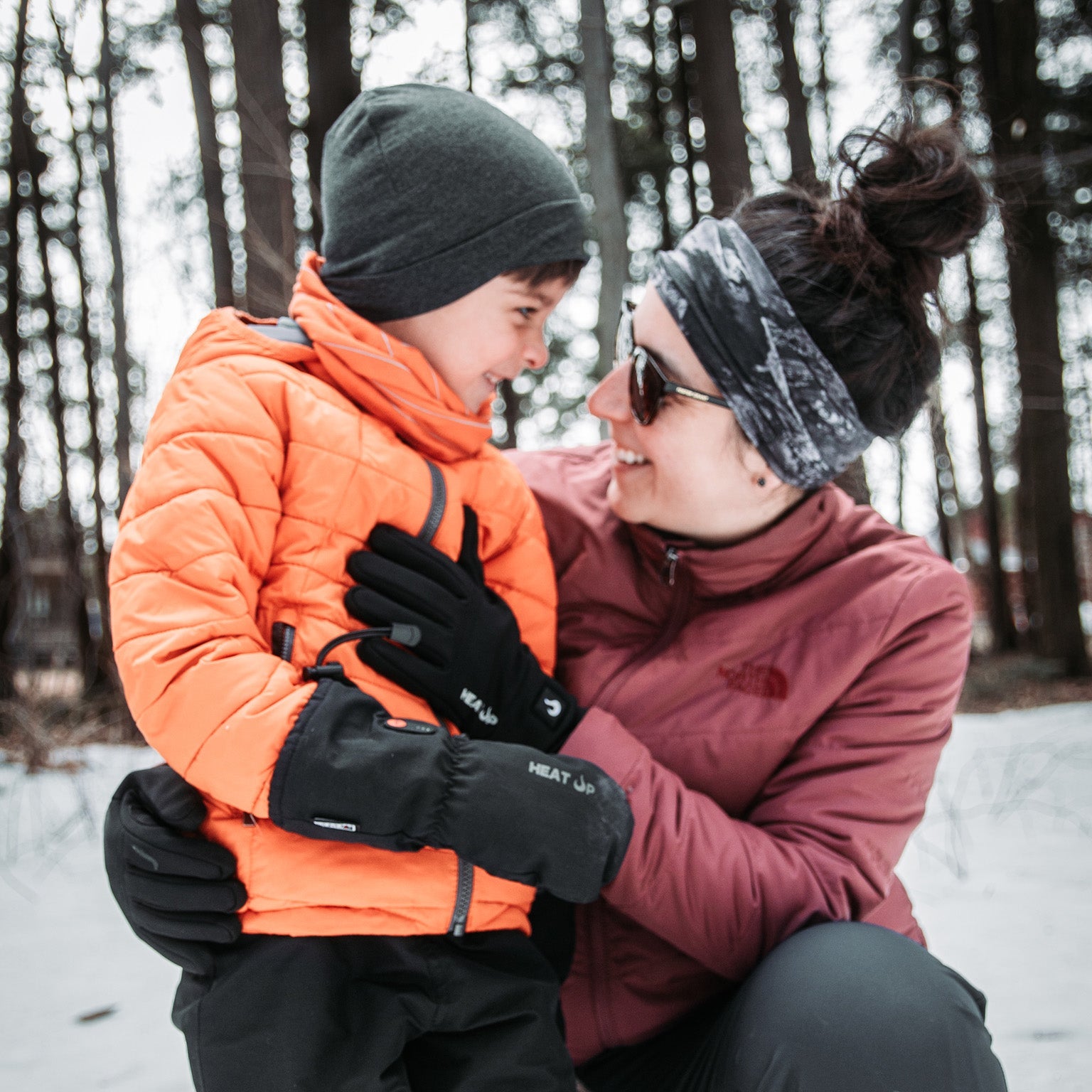 Woman and child in winter clothing outdoors in a snowy forest.