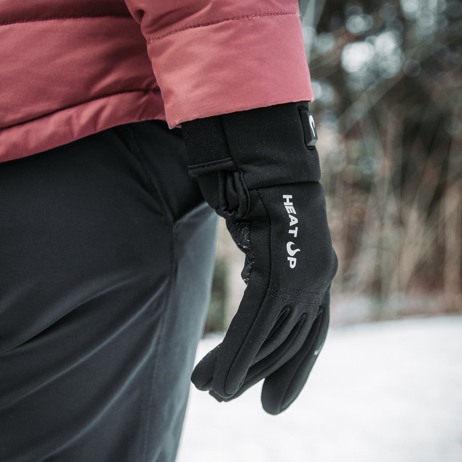 Black glove with 'HEAT UP' branding worn by a person in a snowy outdoor setting.