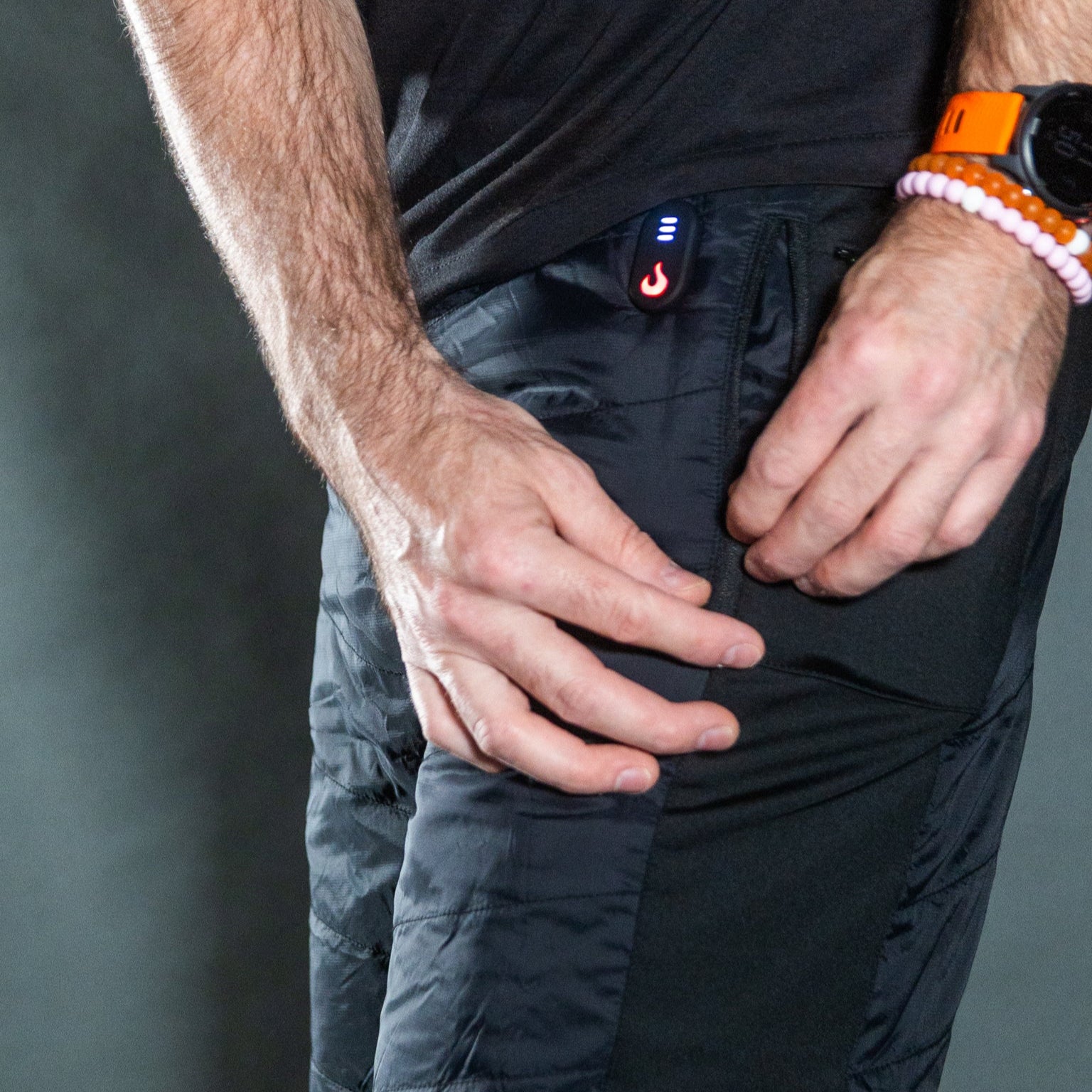 Person wearing black pants with a device on their waistband against a gray background
