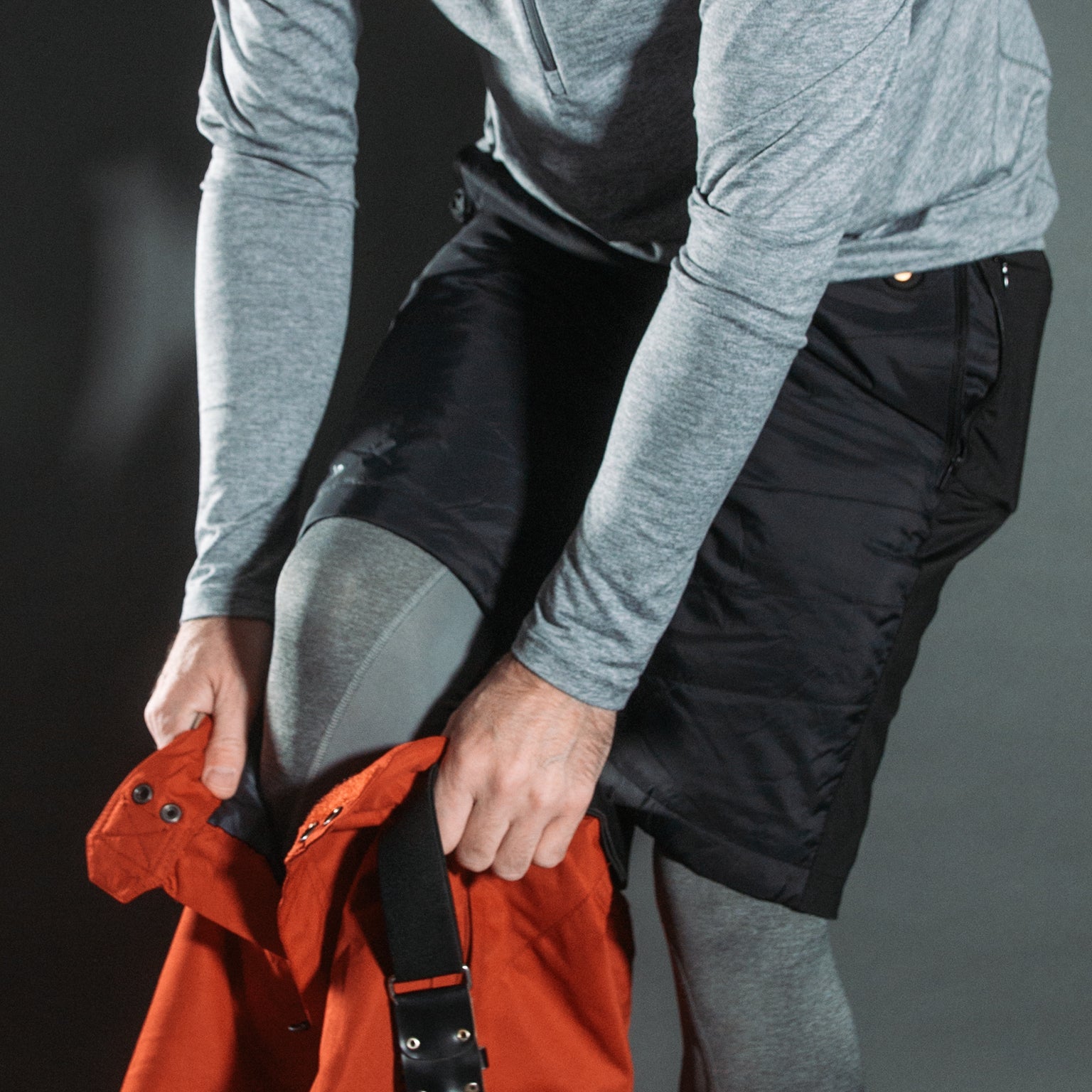 Person holding an orange jacket with a black strap against a gray background