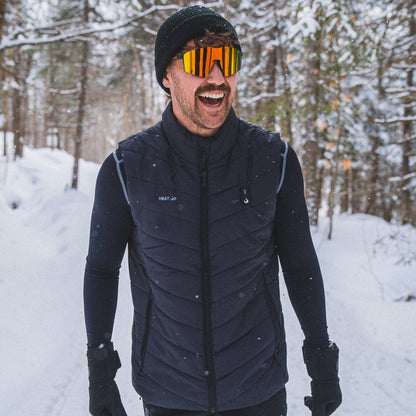 Homme souriant avec des lunettes de sport portant la veste chauffante Heat Up pour homme sur un sentier enneigé