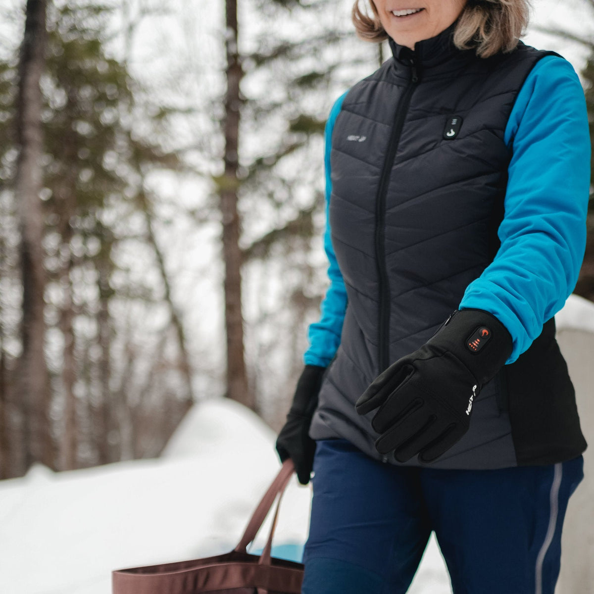 Woman walking in a snowy forest wearing the Heat Up women's heated vest and heated gloves