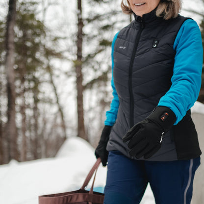 Woman walking in a snowy forest wearing the Heat Up women's heated vest and heated gloves