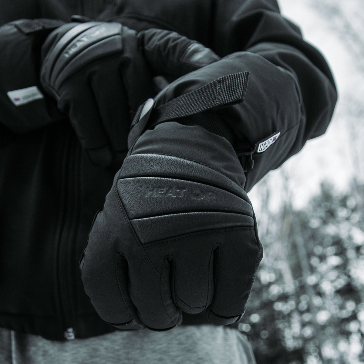 Man in a winter jacket wearing Heat Up Peak heated gloves, snowy forest behind