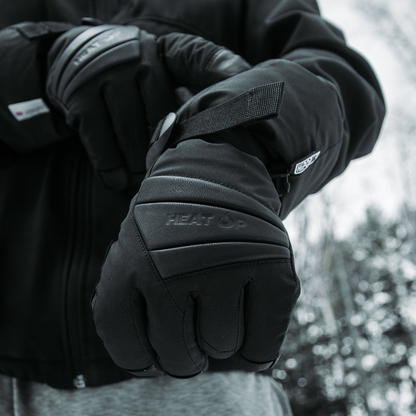Man in a winter jacket wearing Heat Up Peak heated gloves, snowy forest behind